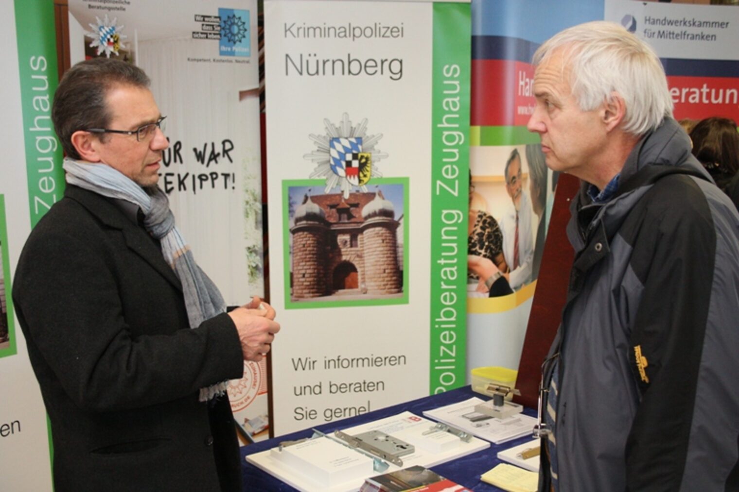 Zwei Männer im Gespräch am Messestand der Kriminalpolizei Nürnberg; einer zeigt auf die Ausstellungswand.