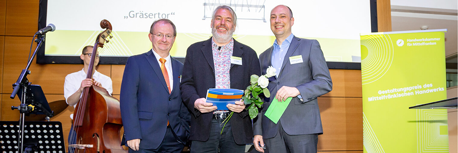 Strahlend nahm Uwe Weber (Mitte) den Gestaltungspreis des Mittelfränkischen Handwerks 2019 entgegen. Mit ihm freuten sich Prof. Dr. Elmar Forster, Hauptgeschäftsführer der Handwerkskammer für Mittelfranken (links) und Laudator Andreas Krieglstein, VR Bank Nürnberg (rechts).