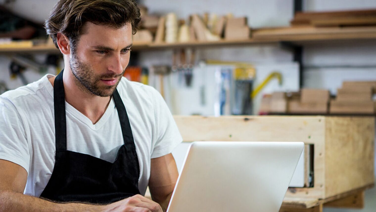 Zu sehen ist ein Handwerker, wie er vor dem Laptop sitzt.