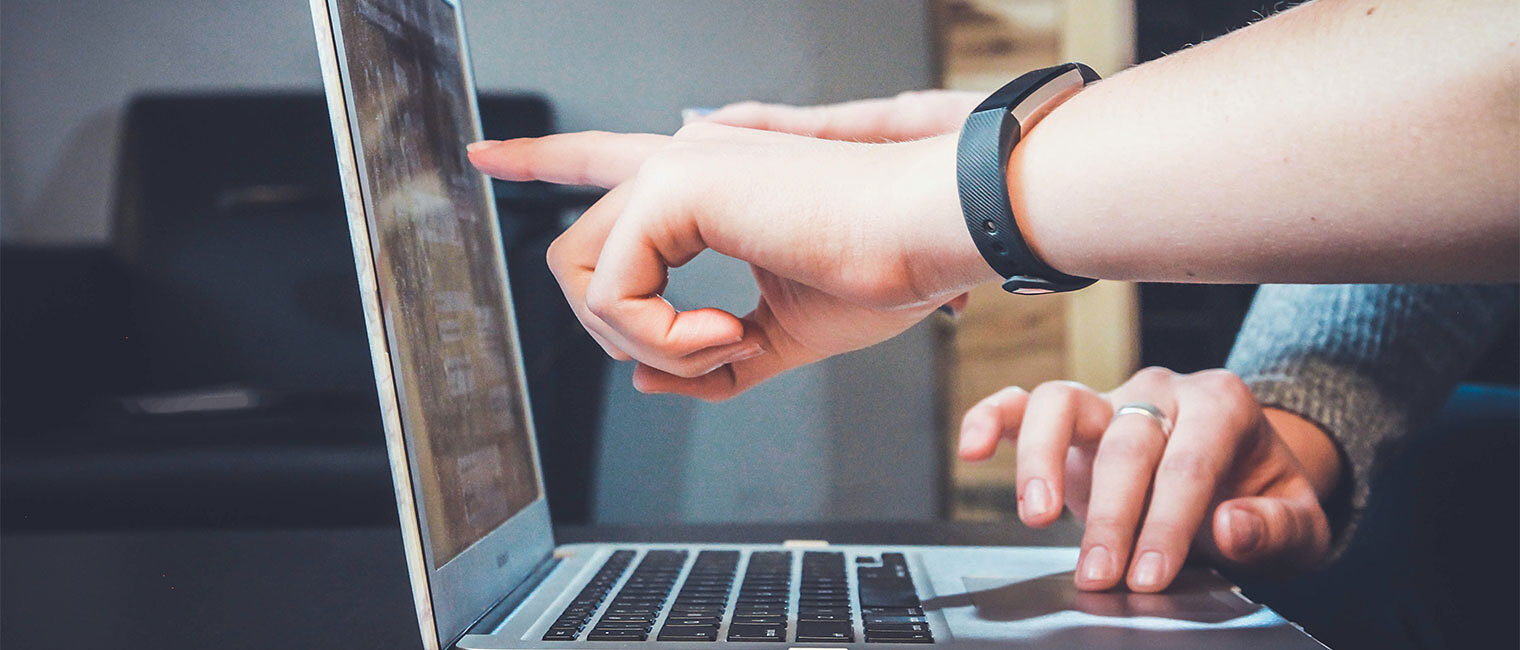 Zu sehen ist eine Hand, die auf einen Laptop-Bildschirm zeigt.