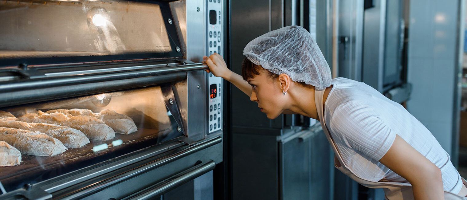 Eine Bäckerin steht vor ihrem Backofen und kontrolliert das gebackene Brot.