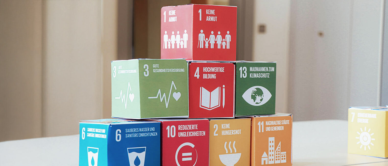 Bausteine der 17 „Sustainable Development Goals“ (SDGs) der UN übereinandergestapelt auf einem Tisch.