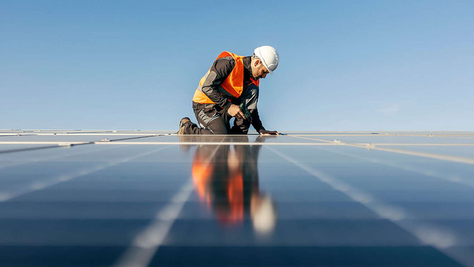 Ein Handwerker bringt auf einem Dach Solarpanelen an.