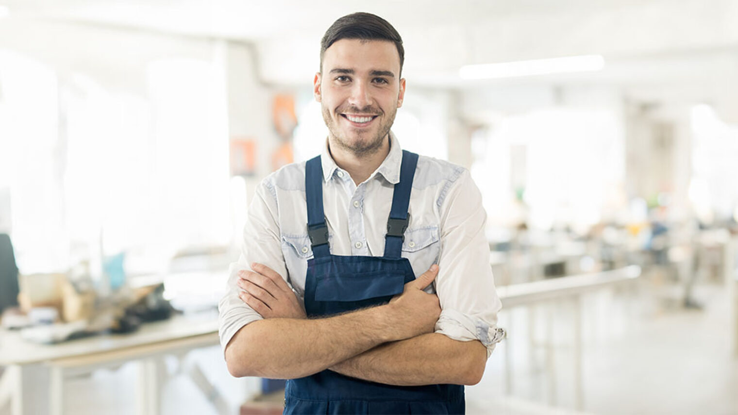 Ein junger Handwerker steht mit verschränkten Armen da und blickt nach vorne.