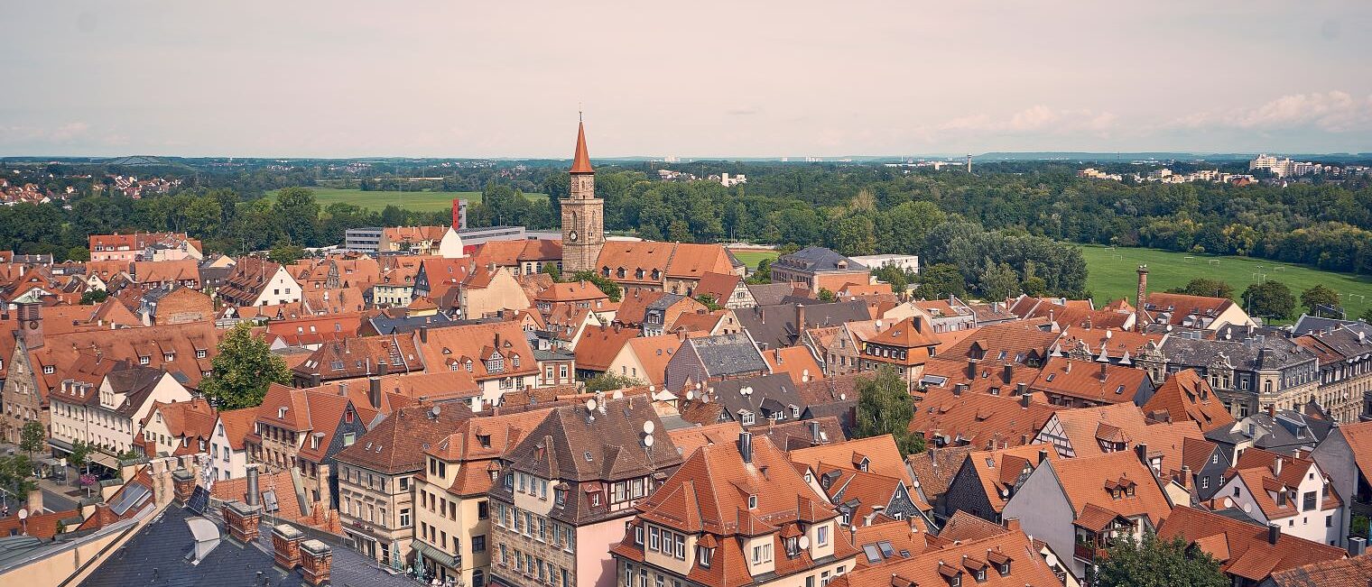 Ausblick auf Fürth vom Rathausturm aus. Dächer und alte Häuser sind zu sehen. Ein Kirchturm. Im Hintergrund Wiesen und Bäume.