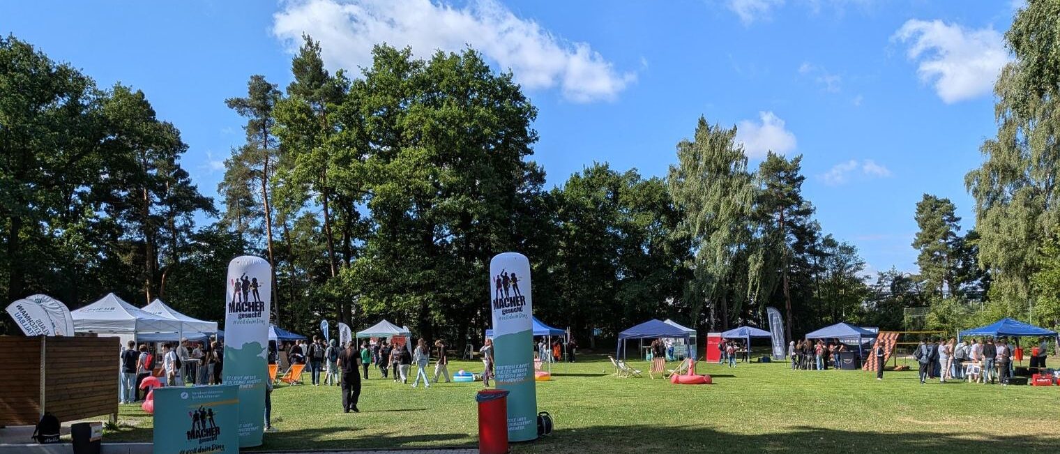 Eine grüne Wiese, viele Stände, zwei große Aufsteller bilden ein Eingangstor