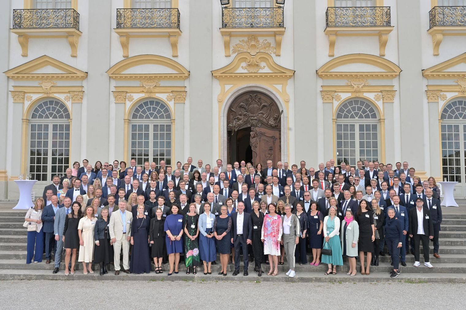 Viele Menschen stehen vor einem eleganten Gebäude auf einer Treppe. 