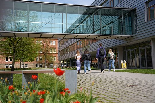 Mehrere Studenten laufen mit dem Rücken zur Kamera über das Gelände der Hochschule Ansbach. 