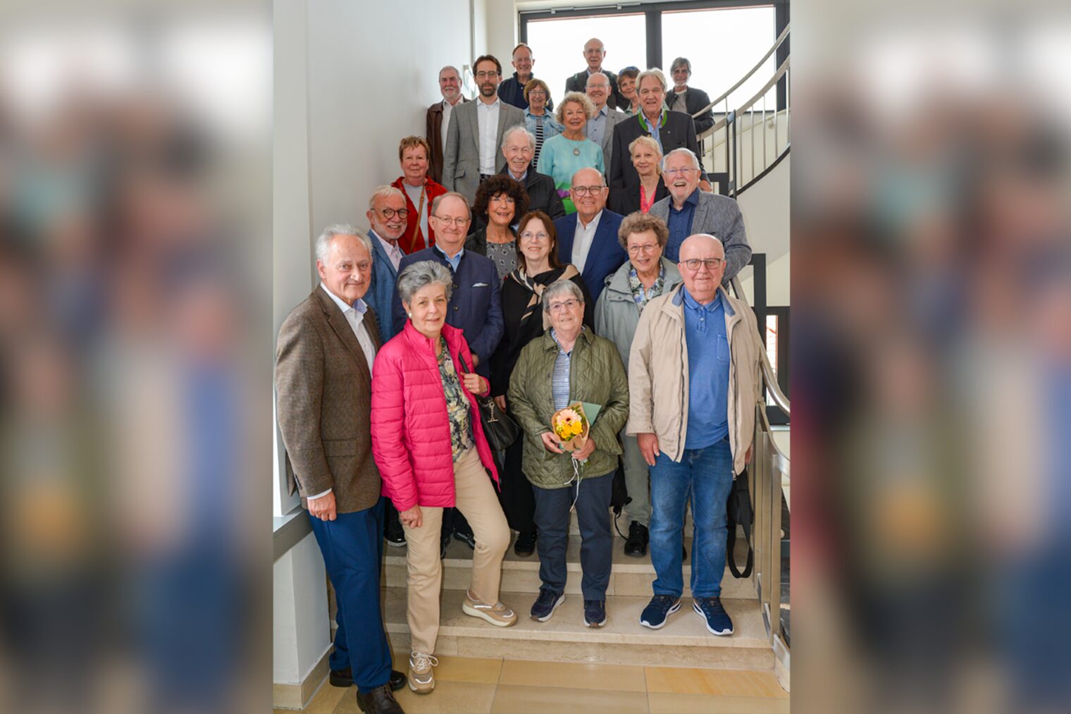 Viele ältere Menschen stehen auf einer Treppe und blicken lachend in die Kamera.