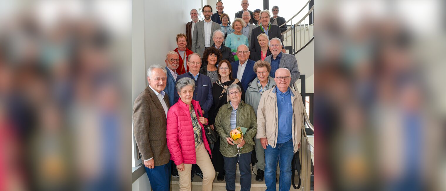 Viele ältere Menschen stehen auf einer Treppe und blicken lachend in die Kamera.