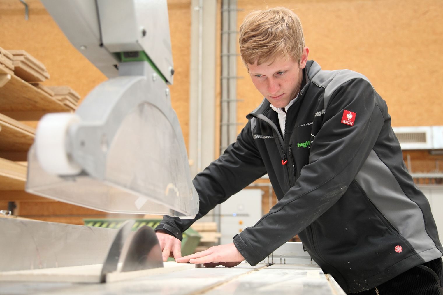 „Auszubildender zum Zimmerer arbeitet konzentriert an einer Tischkreissäge in einer Lehrwerkstatt."