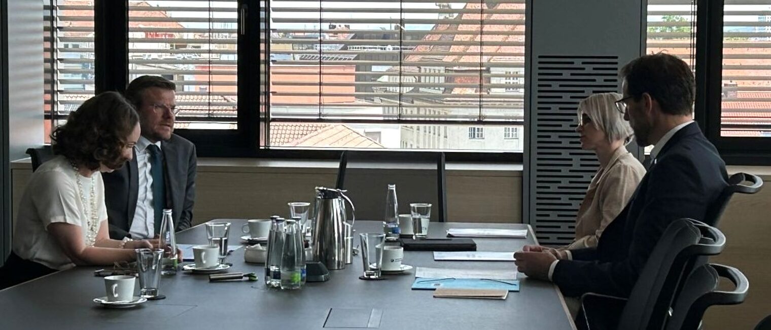 Vier Personen sitzen sich an einem Konferenztisch gegenüber und führen ein Gespräch. 