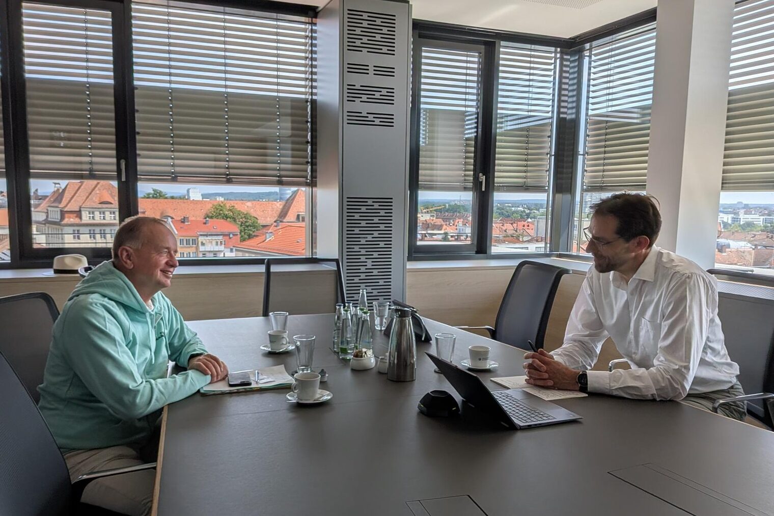 Dr. Rainer-Johannes Wolf und Thomas Deffner sitzen im Gespräch an einem Konferenztisch mit Blick über die Stadt.