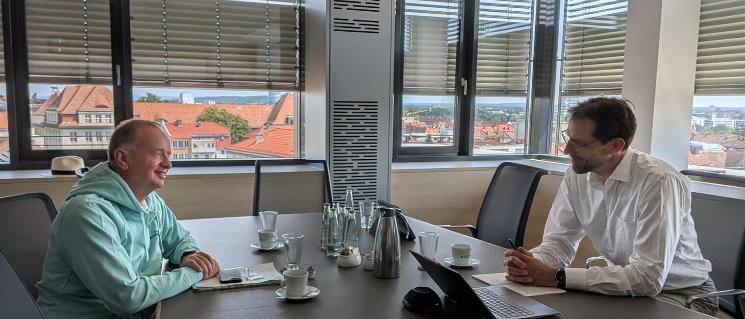 Dr. Rainer-Johannes Wolf und Thomas Deffner sitzen im Gespräch an einem Konferenztisch mit Blick über die Stadt.