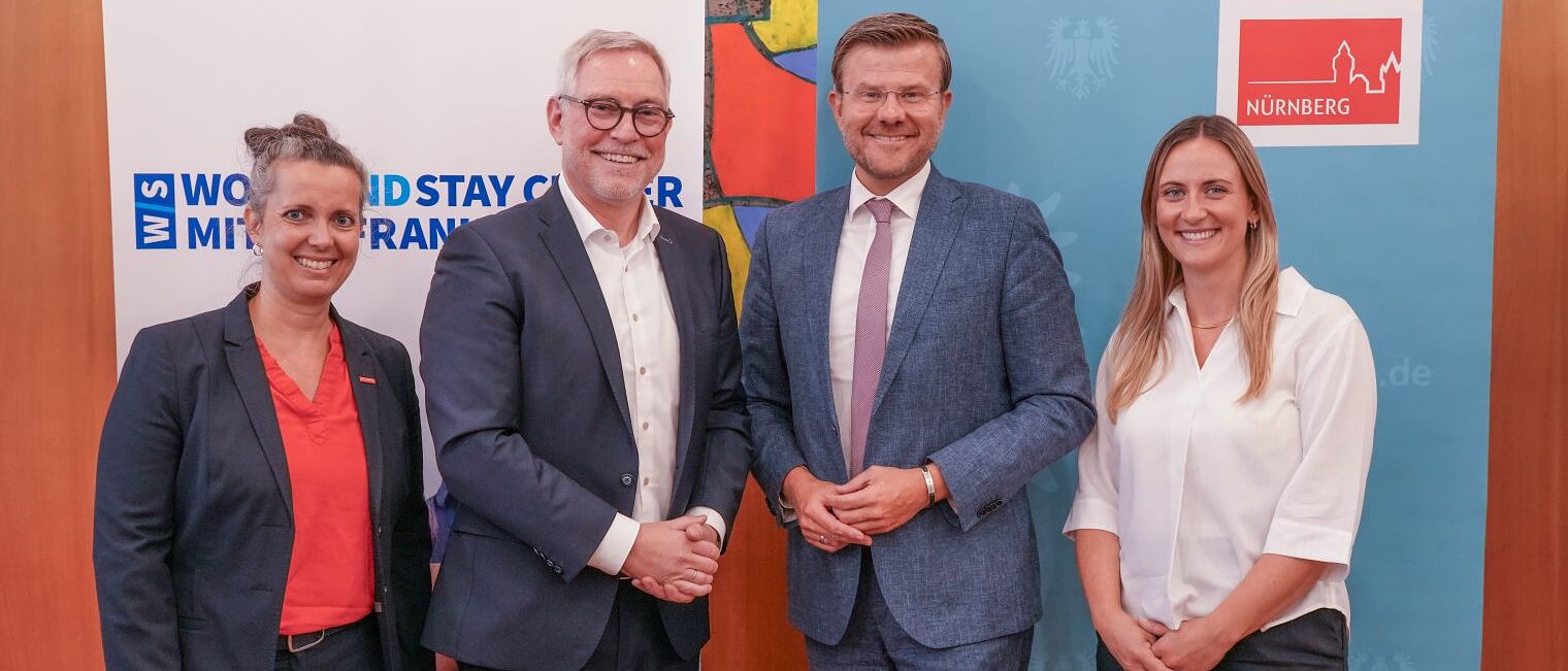 Vier Personen lächeln vor Rollups von Work-and-Stay-Center und Stadt Nürnberg zur Vertragsunterzeichnung.