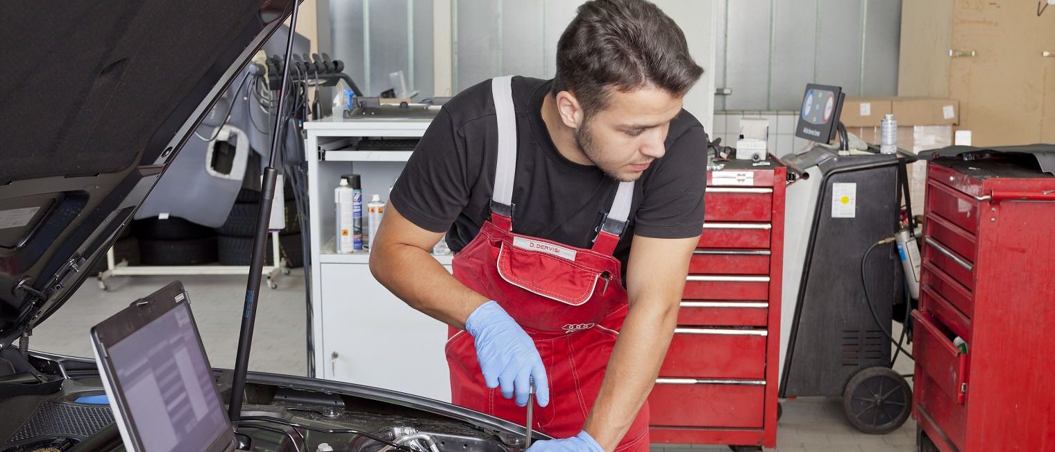 Kfz-Mechatroniker prüft den Motorraum eines Autos und nutzt ein Diagnosegerät in der Werkstatt.